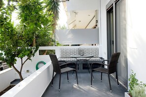 Un balcon avec une table et des chaises, entouré de murs blancs et agrémenté d’un petit arbre.