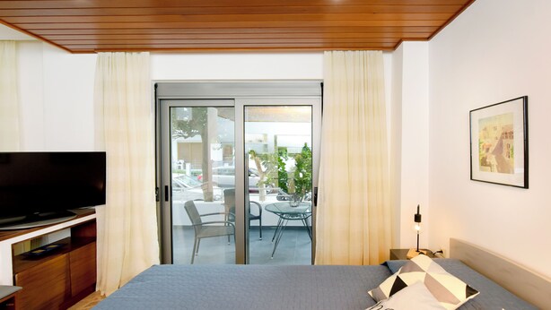 A modern hotel room with a bed, a TV, a balcony with a table and chairs, and a view of the outside. - MARTHA'S HOME. Beautiful and comfortable house in Rhodes. (Rodos)