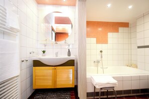 Une salle de bain moderne avec un lavabo blanc, des meubles jaunes, un grand miroir et une baignoire.