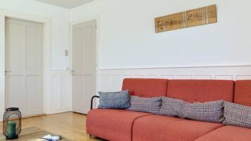 Ein Wohnzimmer mit einem roten Sofa, zwei gemusterten Kissen, einem gewebten Korb und einem kleinen Tisch.