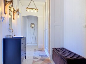 Un couloir avec une commode bleue, un miroir, un luminaire suspendu et un banc.