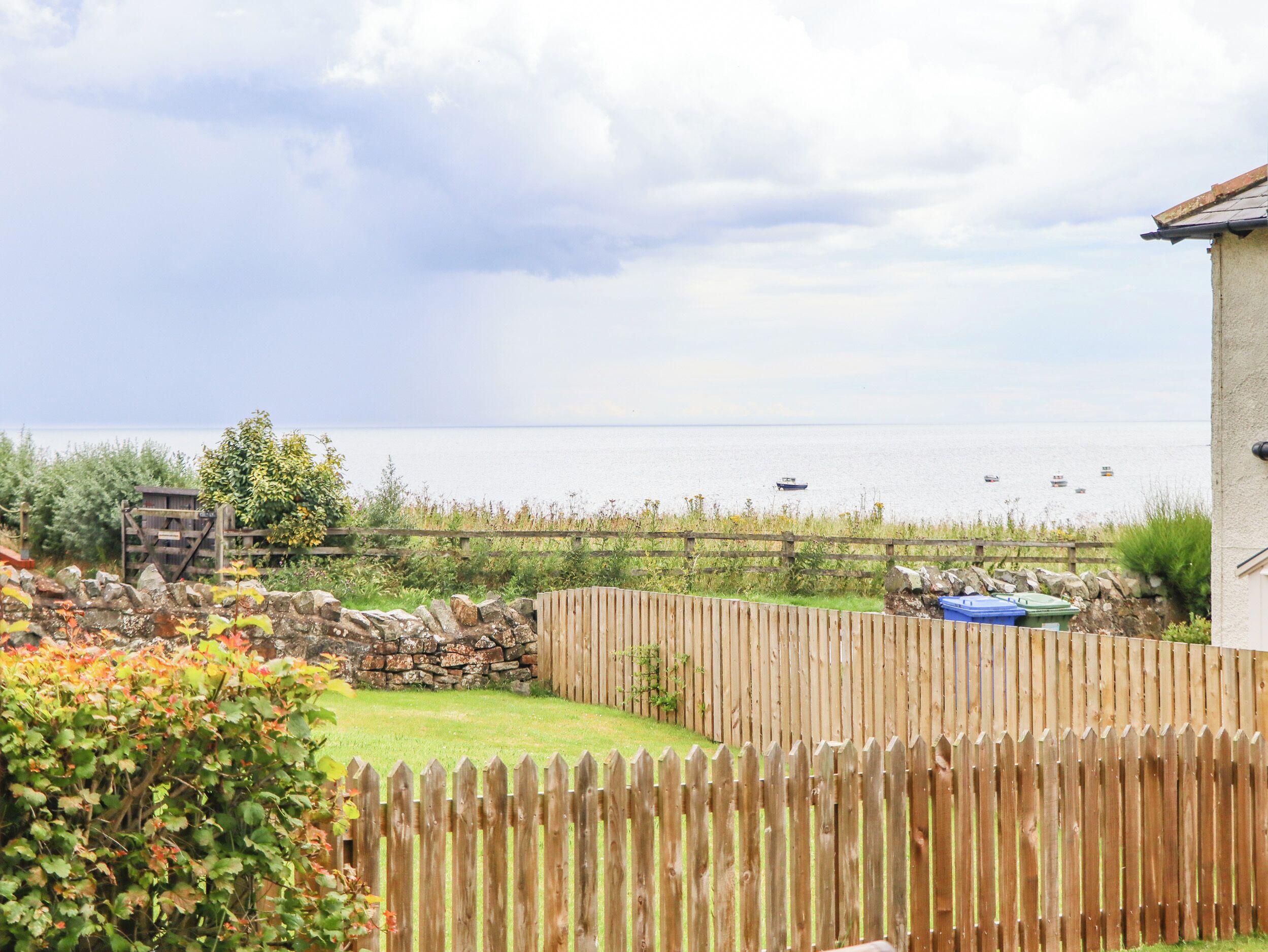 A coastal property with a wooden fence, a stone wall, and a grassy yard.
