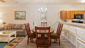 A living room with a sofa, a dining table with chairs, a kitchen area with cabinets and appliances, and a chandelier. - 2 Bedroom- Resort Pool- 1st Floor- Golf (North Myrtle Beach)
