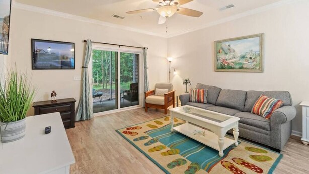 A living room with a sofa, a coffee table, a ceiling fan, a sliding glass door, and a painting on the wall. - 2 Bedroom- Resort Pool- 1st Floor- Golf (North Myrtle Beach)