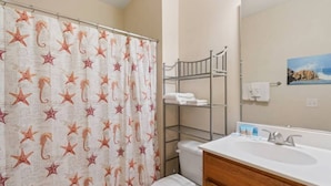 A bathroom with a shower curtain featuring starfish and seahorse patterns, a white sink with a mirror, and a bunk bed with white towels. - 2 Bedroom- Resort Pool- 1st Floor- Golf (North Myrtle Beach)