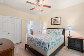 A bedroom with a bed, nightstands, a ceiling fan, and a door leading to another room.