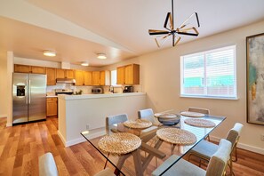 A modern kitchen with wooden cabinets, a stainless steel refrigerator, and a dining area with a glass table and woven placemats. - ★ Modern LUX 4 bdrm - Near Mall, Boeing, Paine Field & Eateries! ★ (Everett)