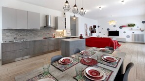 Uma cozinha moderna com armários cinza, uma ilha central e um espaço de refeições para seis pessoas, com pratos vermelhos e brancos.