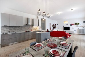 Ett modernt kök med grå skåp, en köksö och en matplats med plats för sex personer, där bordet är dukat med röda och vita tallrikar.