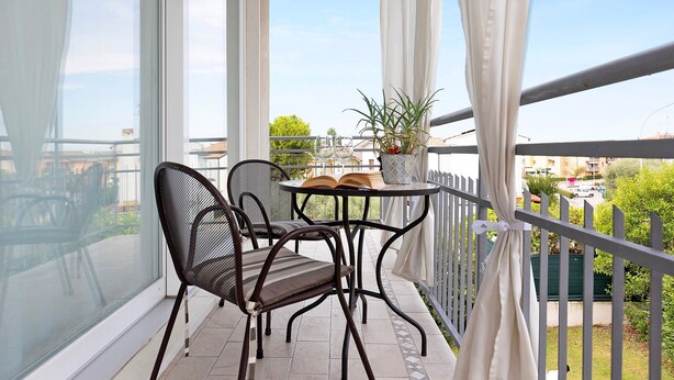 Varanda com mesa, cadeiras, planta em vaso e vista da cidade.