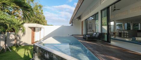A modern house with a swimming pool, a patio with outdoor furniture, and a large glass door leading to a spacious interior.