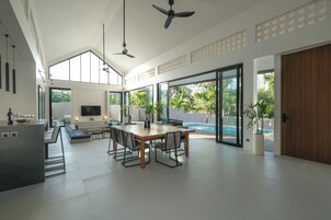 Uma sala de estar espaçosa com uma mesa de jantar, sofás e uma televisão. Há uma janela grande com vista para o exterior.