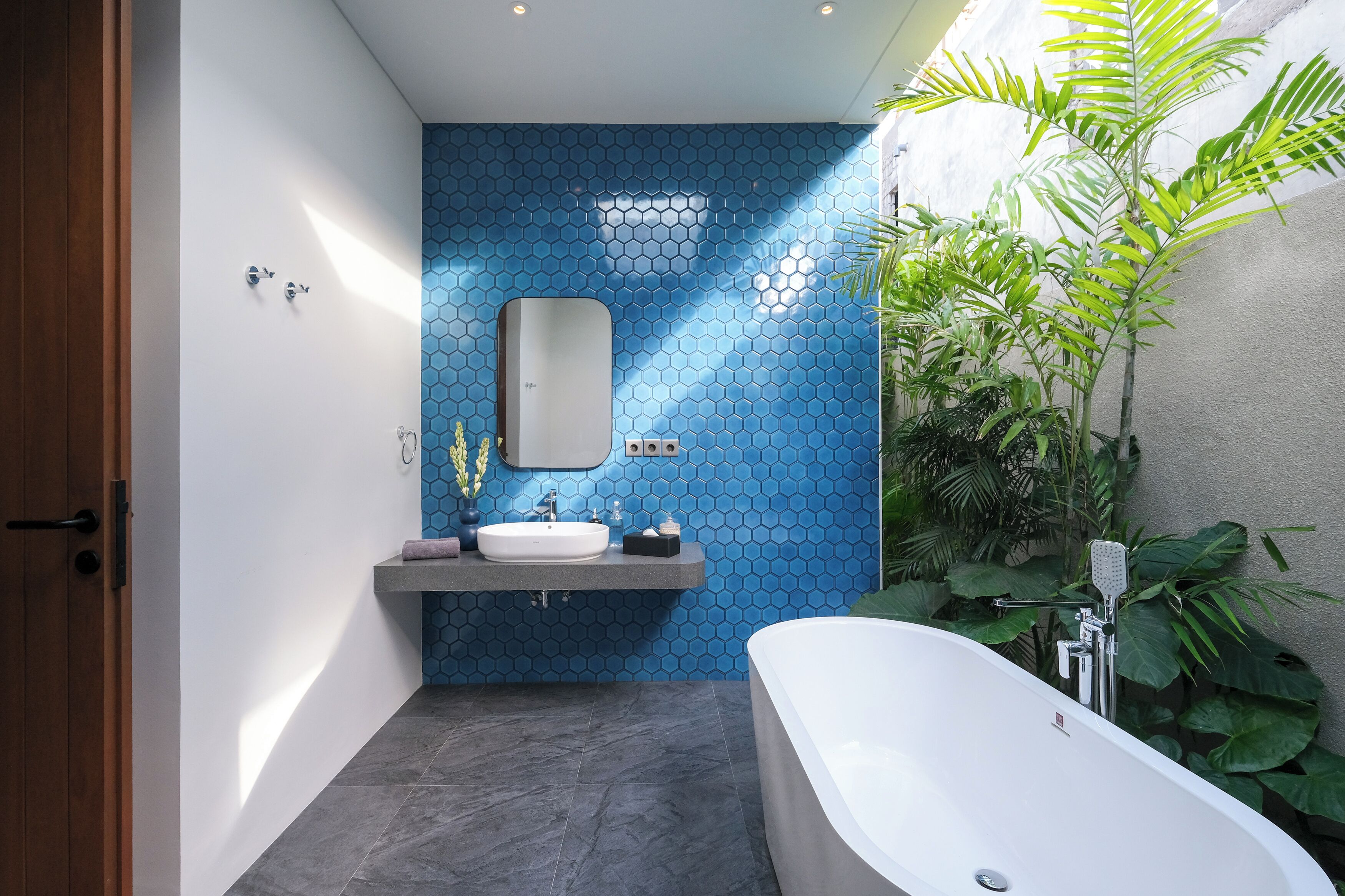 A modern bathroom with a blue hexagonal tile wall, a white bathtub, and a vanity with a mirror.
