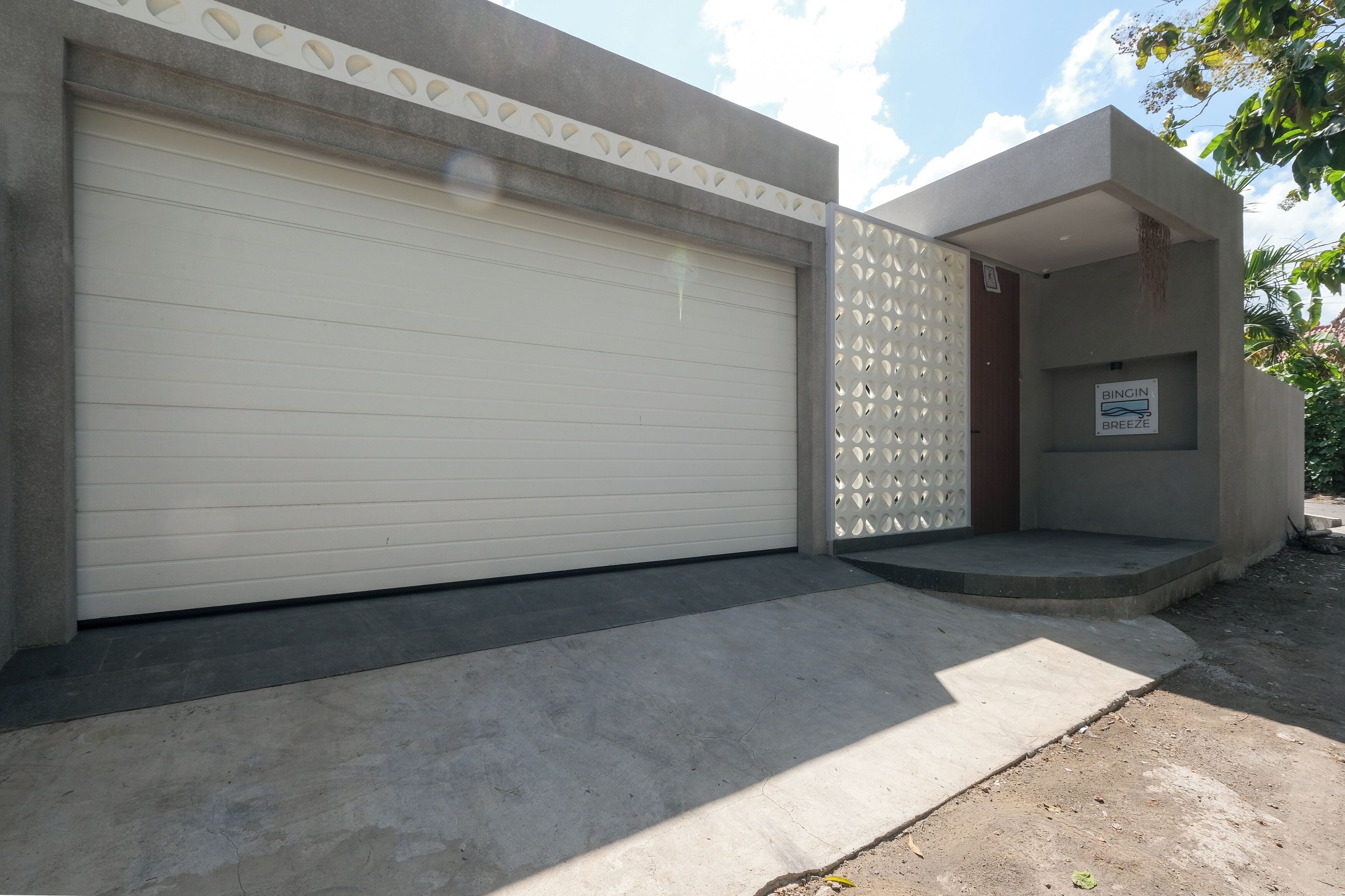 Um edifício moderno com uma porta de garagem fechada, uma pequena entrada com degraus e uma placa com a inscrição 'BINGIN BREEZE'.