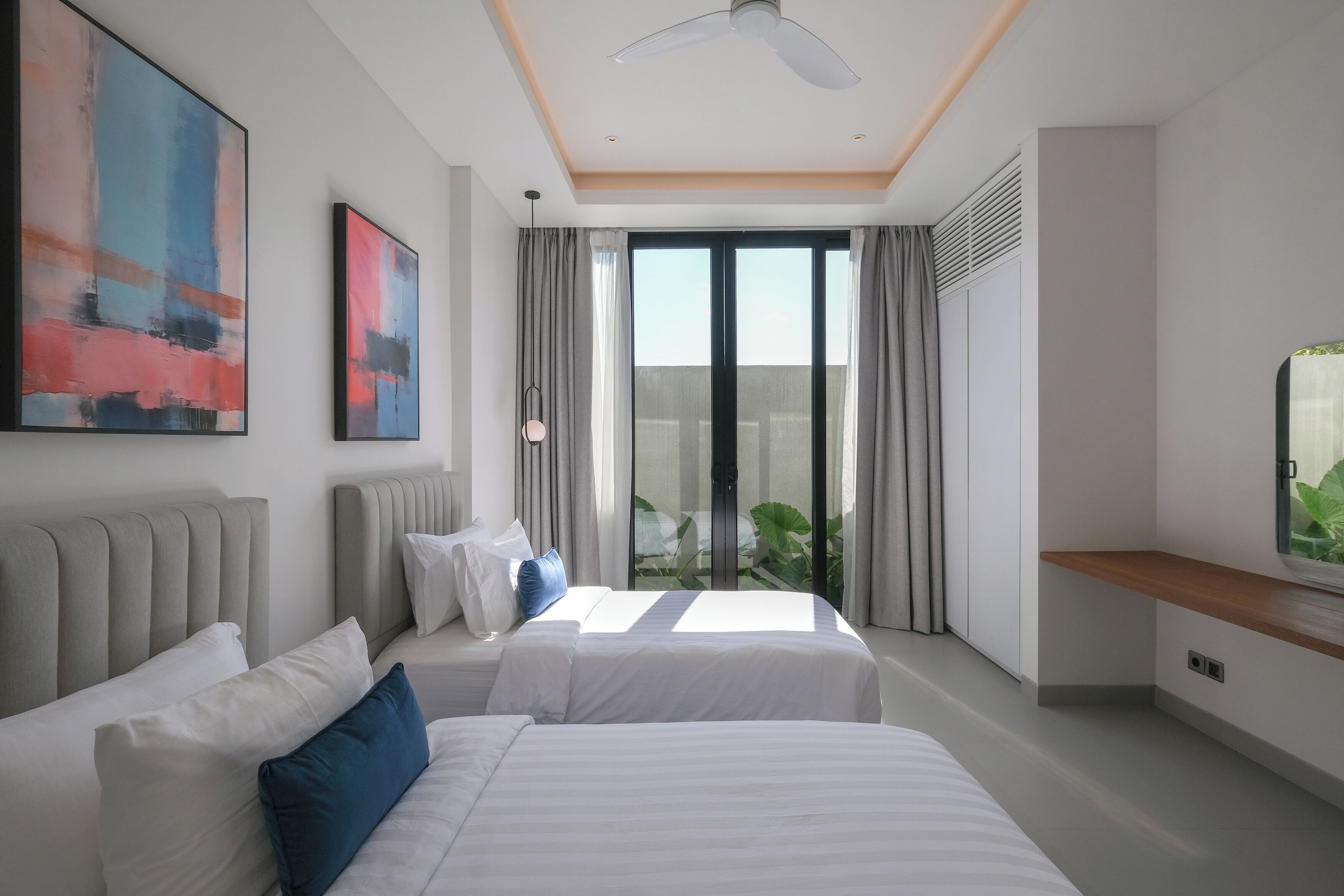 Une chambre d’hôtel moderne équipée de deux lits, d’un ventilateur de plafond, d’une grande fenêtre avec des rideaux et d’un téléviseur à écran plat.