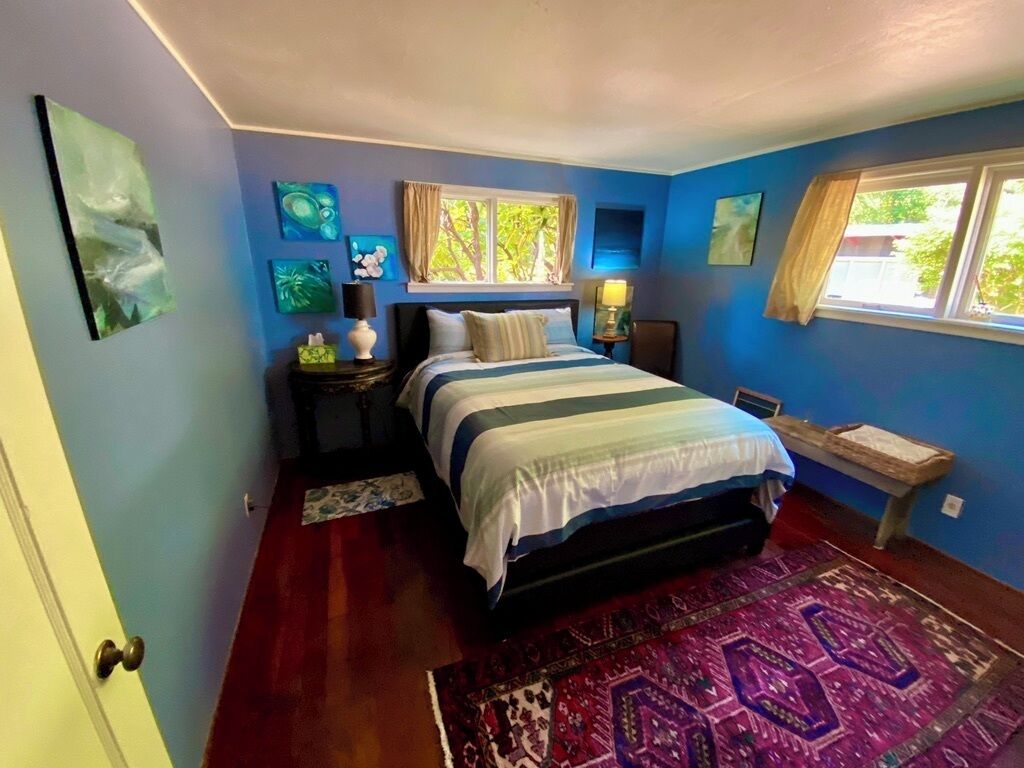 Un dormitorio con cama, mesita de noche, lámpara, ventana y obras de arte en las paredes.