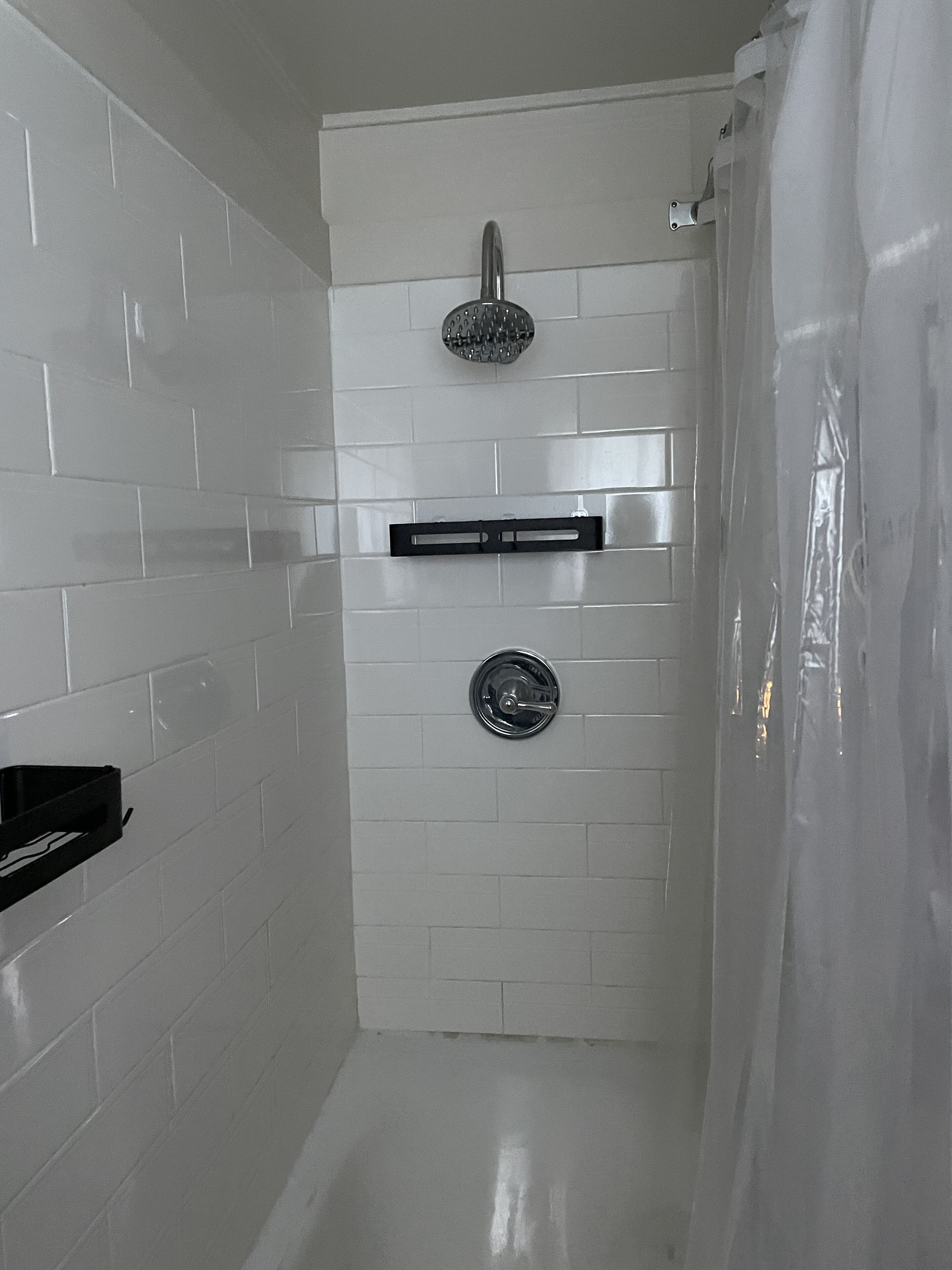 A bathroom with white tiled walls, a shower, and a black towel rack.