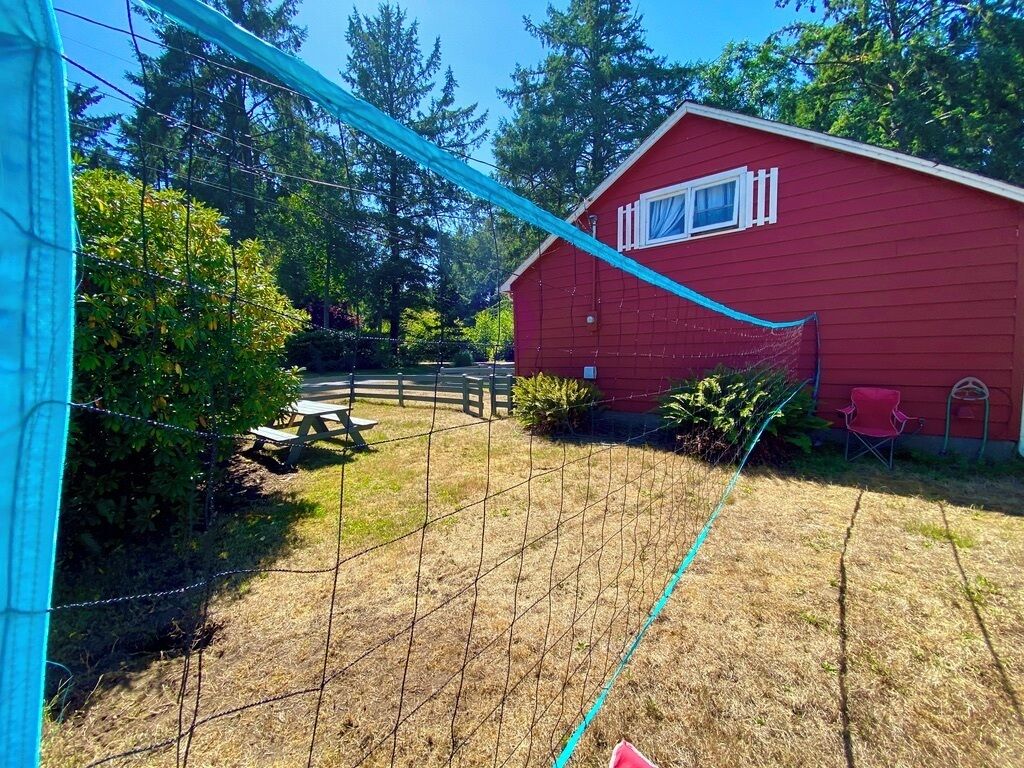 A red building with a window, surrounded by a fenced yard with a picnic table and a chair.