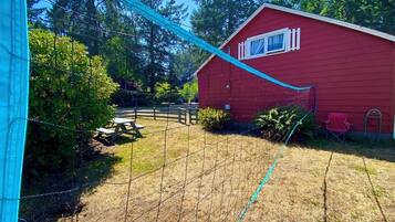 A red building with a window, surrounded by a fenced yard with a picnic table and a chair.