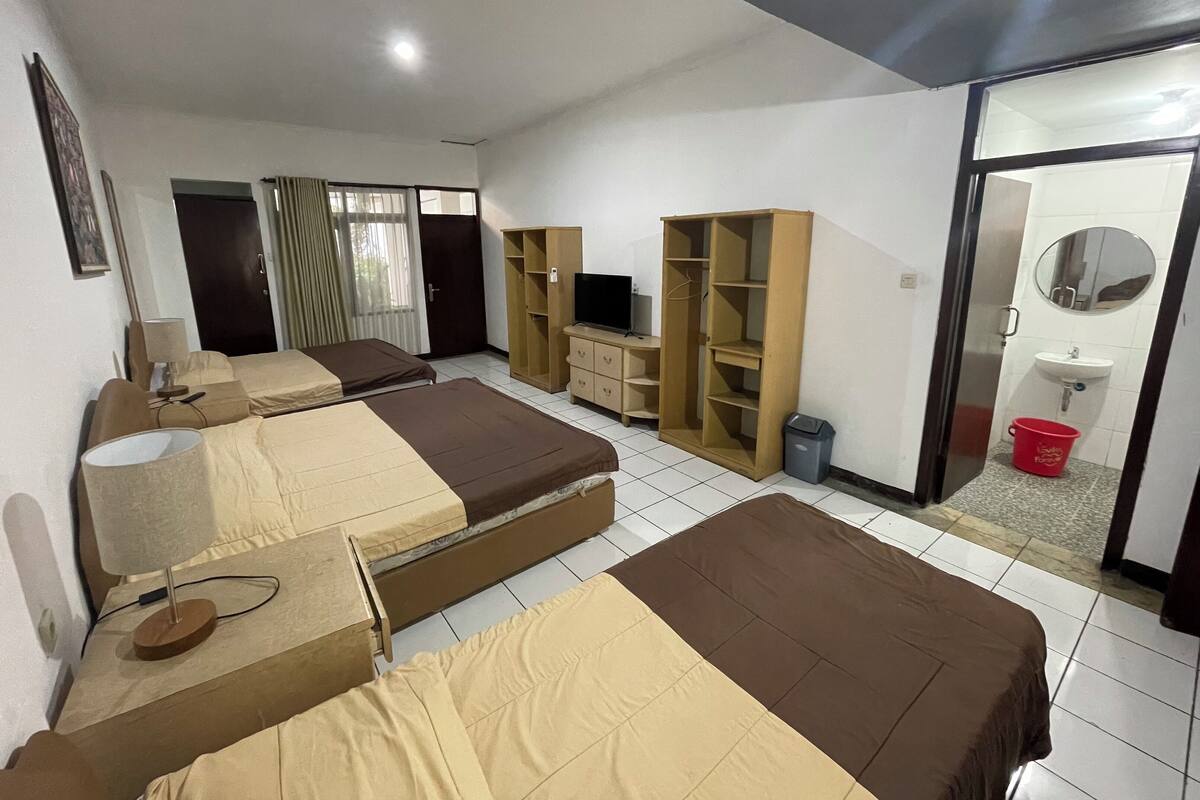 A hotel room with two beds, a TV, a wardrobe, a desk, and a bathroom with a sink and mirror.