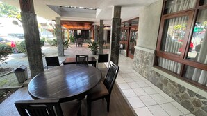 An outdoor patio area with a round table and chairs, stone pillars, and a view of the street. - Hotel Gegerkalong Asri (Bandung)