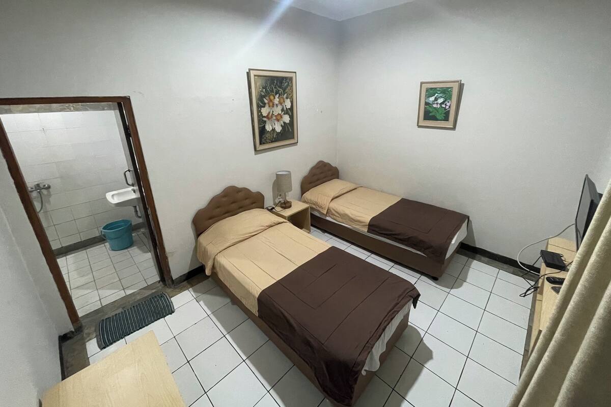 A small, clean room with two beds, a sink, and a shower.