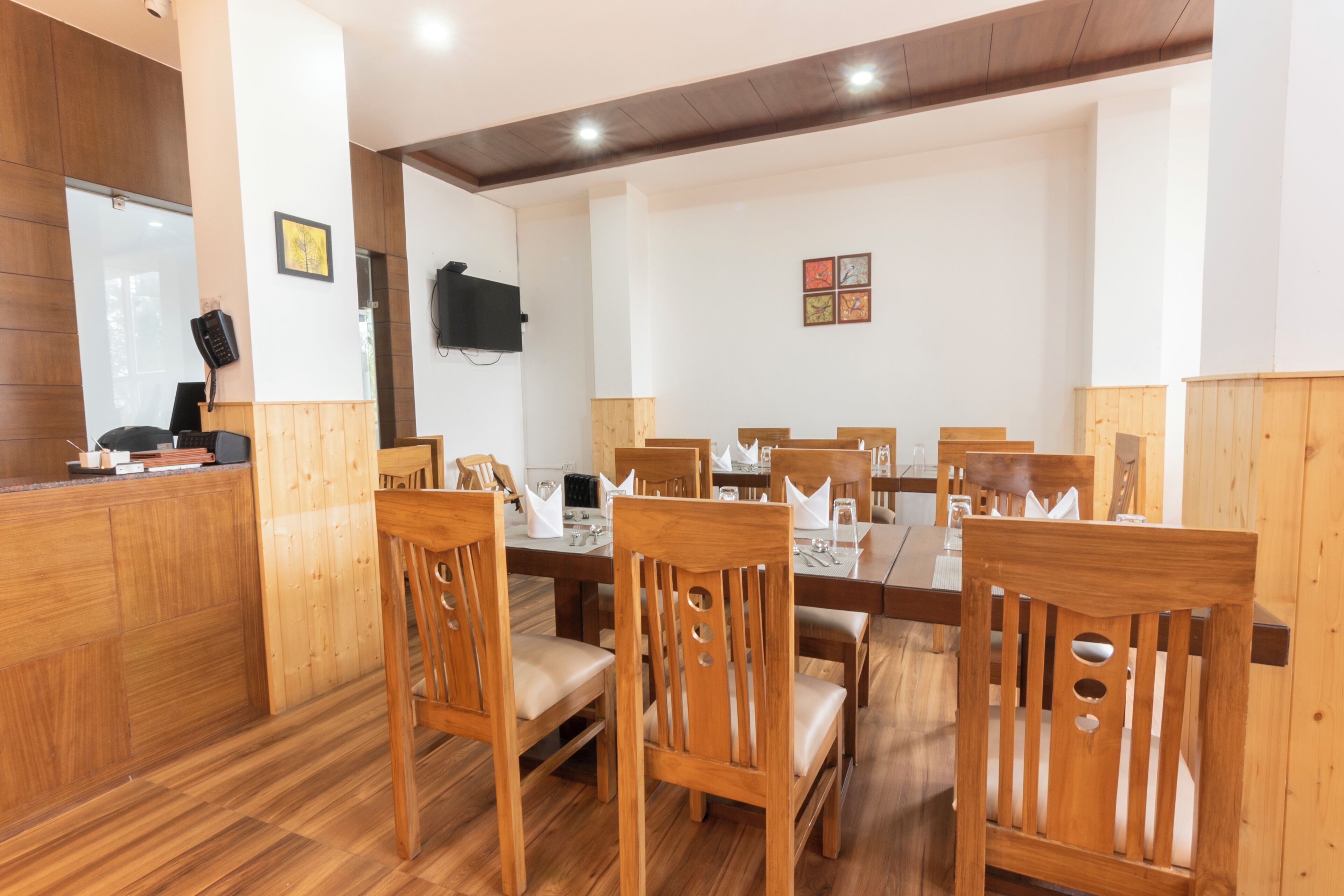 A dining area with wooden furniture, a TV mounted on the wall, and a counter with a cash register.