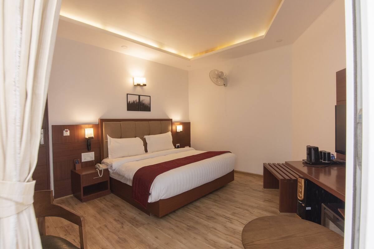 Una habitación de hotel con una cama grande, mesitas de noche, un escritorio y un televisor.