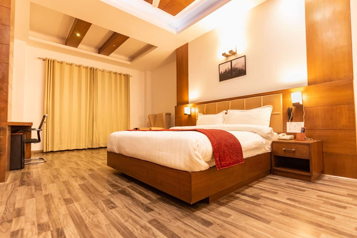 Una cama grande y céntrica con cabecera de madera, flanqueada por mesitas de noche con lámparas. Se ve una ventana grande con cortinas al fondo.