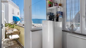 Una cocina compacta con refrigerador, cafetera y un pequeño ventanal con vista al mar.