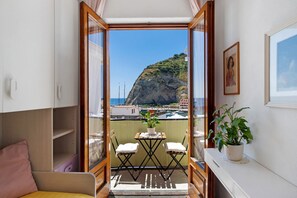 Un balcon donnant sur une falaise et un port de plaisance, une petite table avec des chaises et une plante en pot.