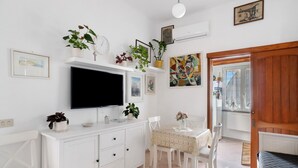 Una habitación con televisión, muebles blancos, una mesa de comedor, sillas y una cama.