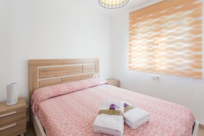 Ein ordentlich bezogenes Bett mit einem gemusterten Überwurf, einem Holz-Kopfteil, einem Nachttisch mit Lampe und einem an der Wand hängenden Kunstwerk.