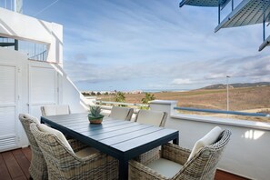 Un balcone con tavolo e sedie, affacciato su un paesaggio con campi e colline lontane.