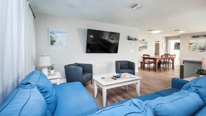 A modern living room with blue sofas, a white coffee table, and a flat-screen TV mounted on the wall.