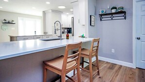 A modern kitchen with white cabinetry, a large island with two wooden chairs, and a built-in oven.