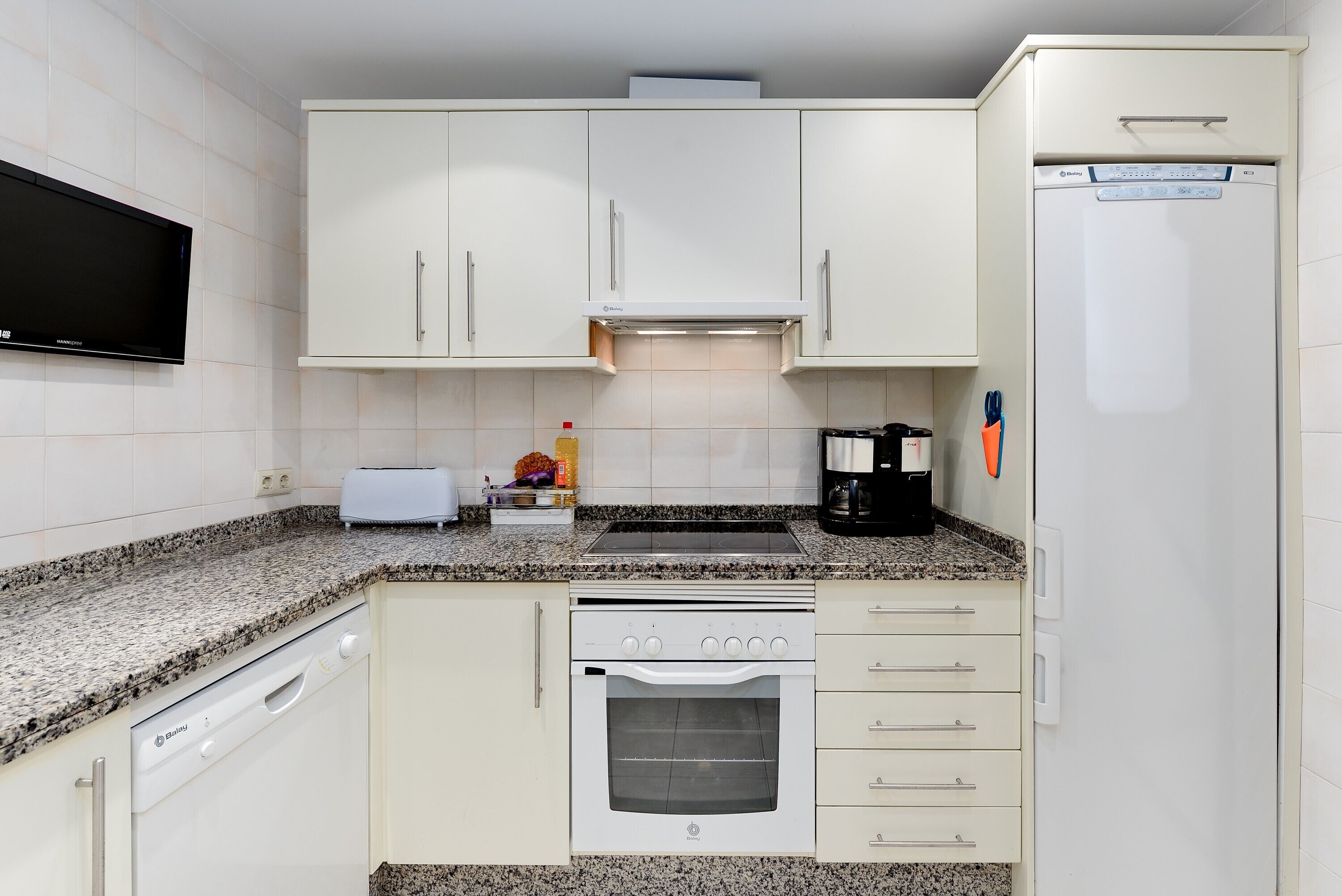 A kitchen with white cabinets, a built-in oven, a dishwasher, a coffee maker, and a microwave.