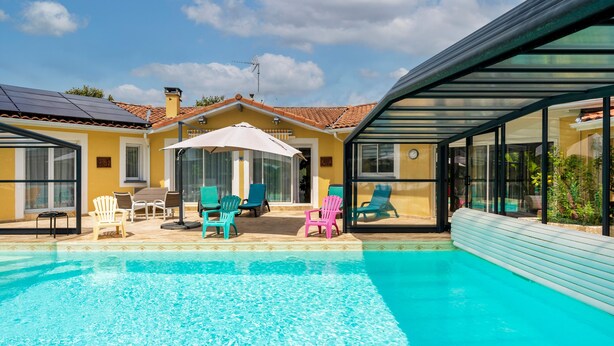 A swimming pool with lounge chairs, a covered patio, and a house with a tiled roof. - Large Family Villa with Private Heated Pool in Landes (Clermont)