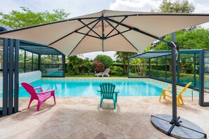 A swimming pool with a covered area, chairs, and a glass-enclosed structure.