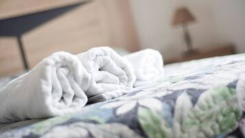 Un asciugamano bianco e ordinato su un letto con una coperta a motivi floreali.