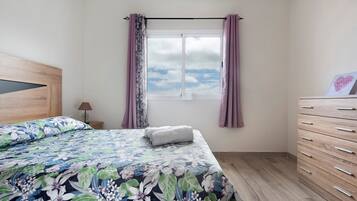 Ein Schlafzimmer mit Bett, Fenster mit Vorhängen, Nachttisch mit Lampe und Kommode.