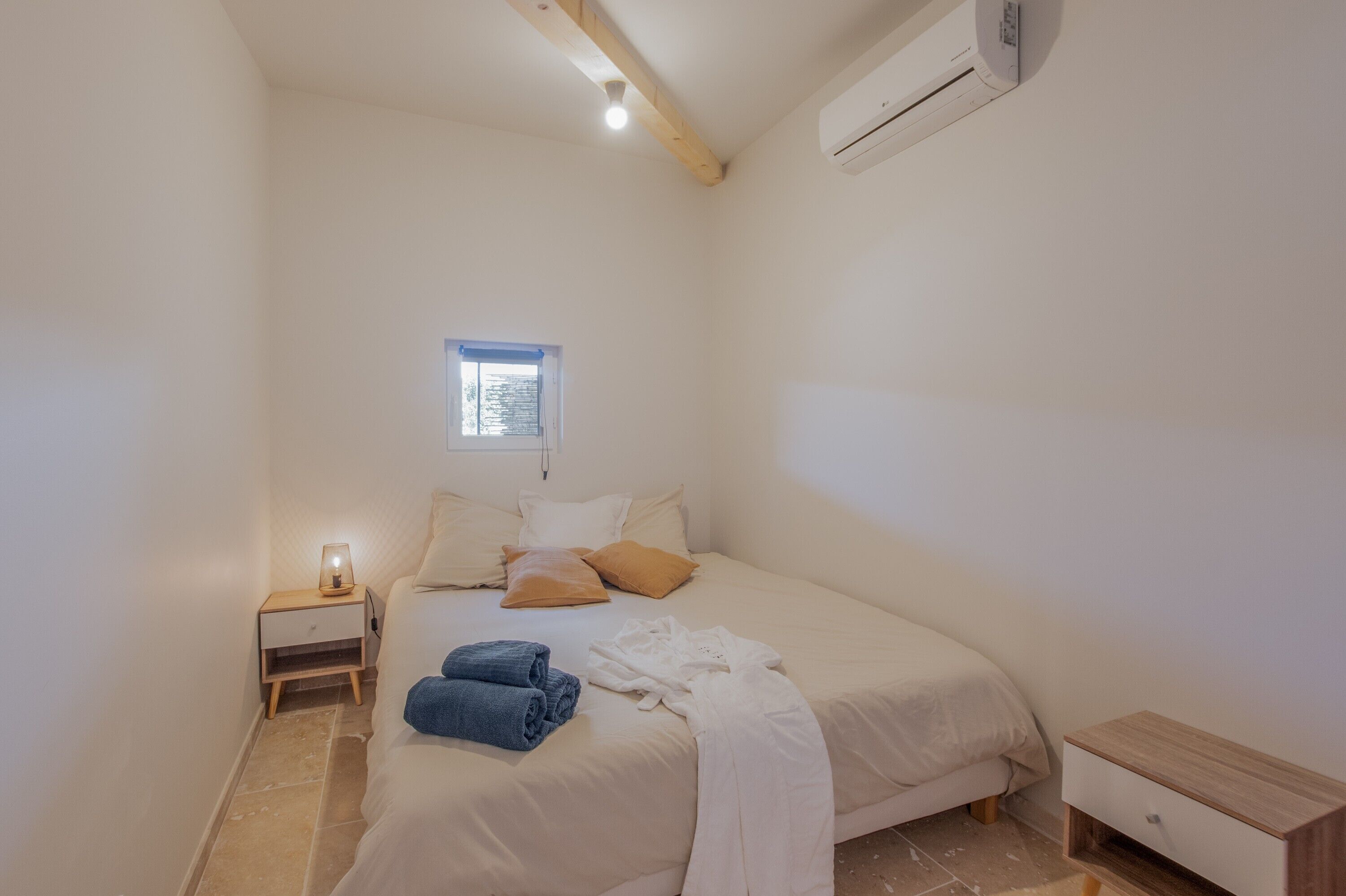 Ein Schlafzimmer mit Bett, Nachttisch, Fenster und Klimaanlage.