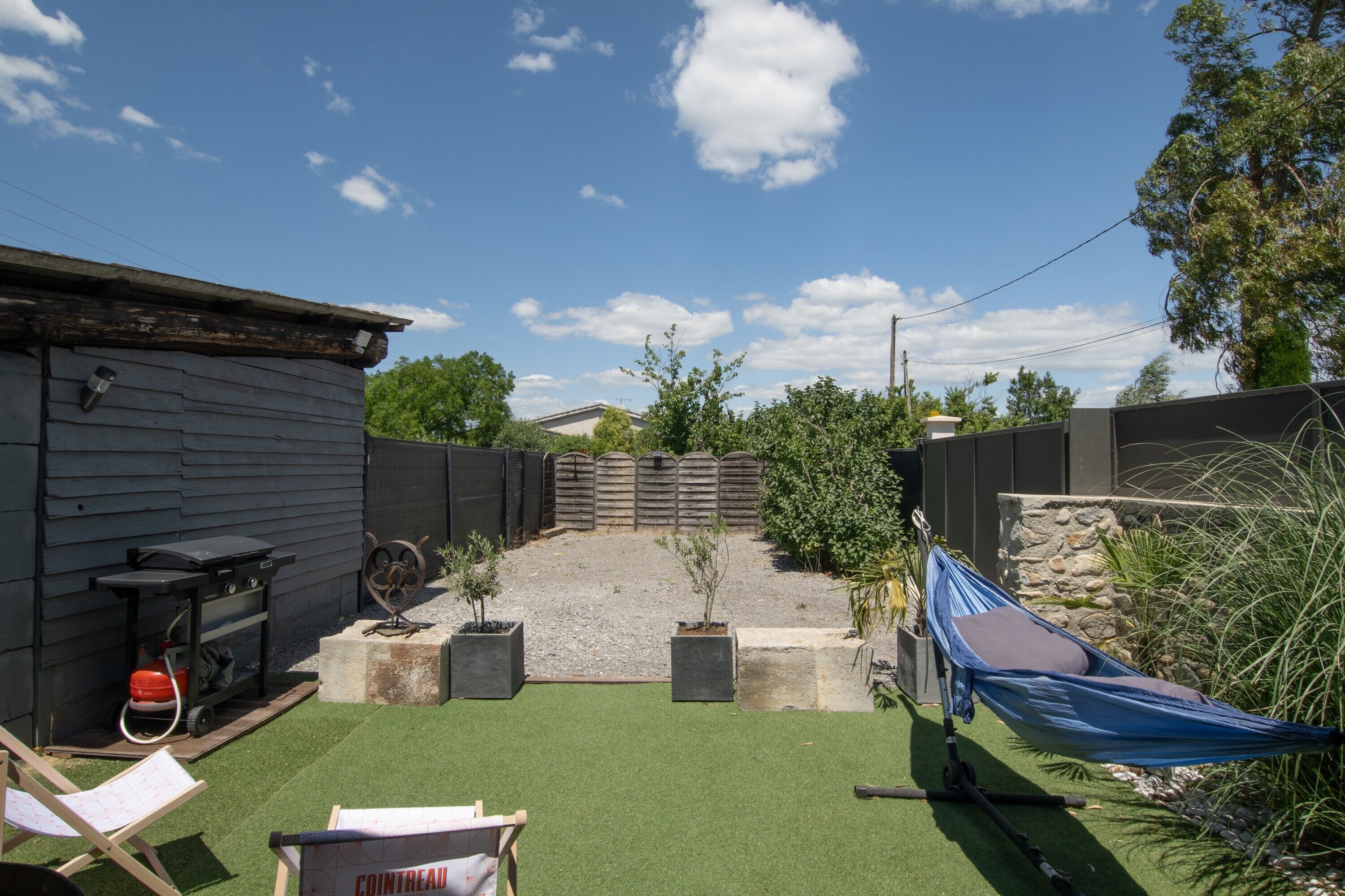 A backyard with artificial grass, a barbecue grill, a hammock, and a fenced area.