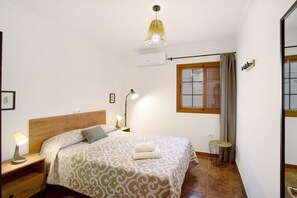 Una camera da letto con un letto, lampade da comodino, un tavolino rotondo, una finestra con tende e un condizionatore d'aria.