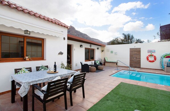 Un patio con piscina, un tavolo da pranzo con sedie e un piccolo giardino.