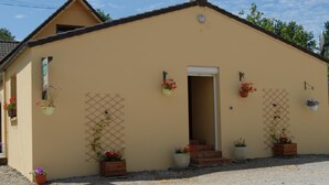 Ein eingeschossiges Gebäude mit hellbeiger Fassade, einem kleinen Eingang und Topfpflanzen.