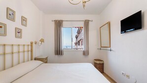 A bedroom with a bed, a TV, a window with curtains, a wall-mounted mirror, and framed pictures.