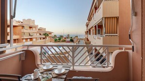 A balcony with a view of the sea, a table with cups and a pitcher, and buildings in the background.
