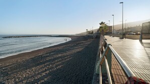 A coastal walkway with a paved path, a railing, and a view of the beach and ocean.