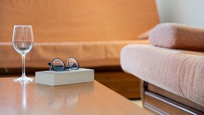 A wooden table with a book and glasses, a glass of water, and a brown sofa in the background.